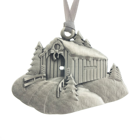 A covered bridge coated in snow. Christmas Tree ornament. Made from Pewter. Silver ribbon. Made in Fredericton NB New Brunswick Canada