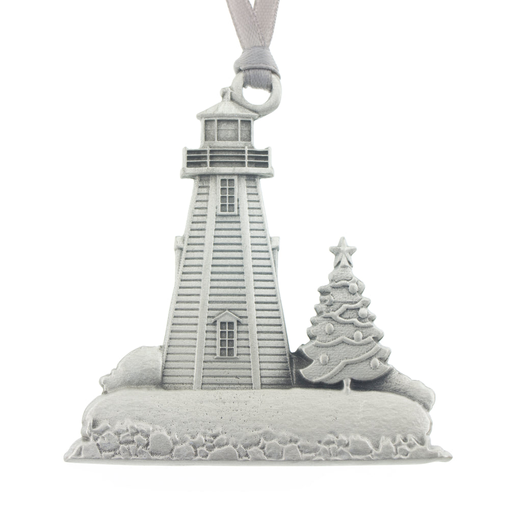 A bucolic scene of a lighthouse with a Christmas tree on a snow covered shore. Peggy's Cove. Christmas Tree ornament. Made from Pewter. Silver ribbon. Made in Fredericton NB New Brunswick Canada