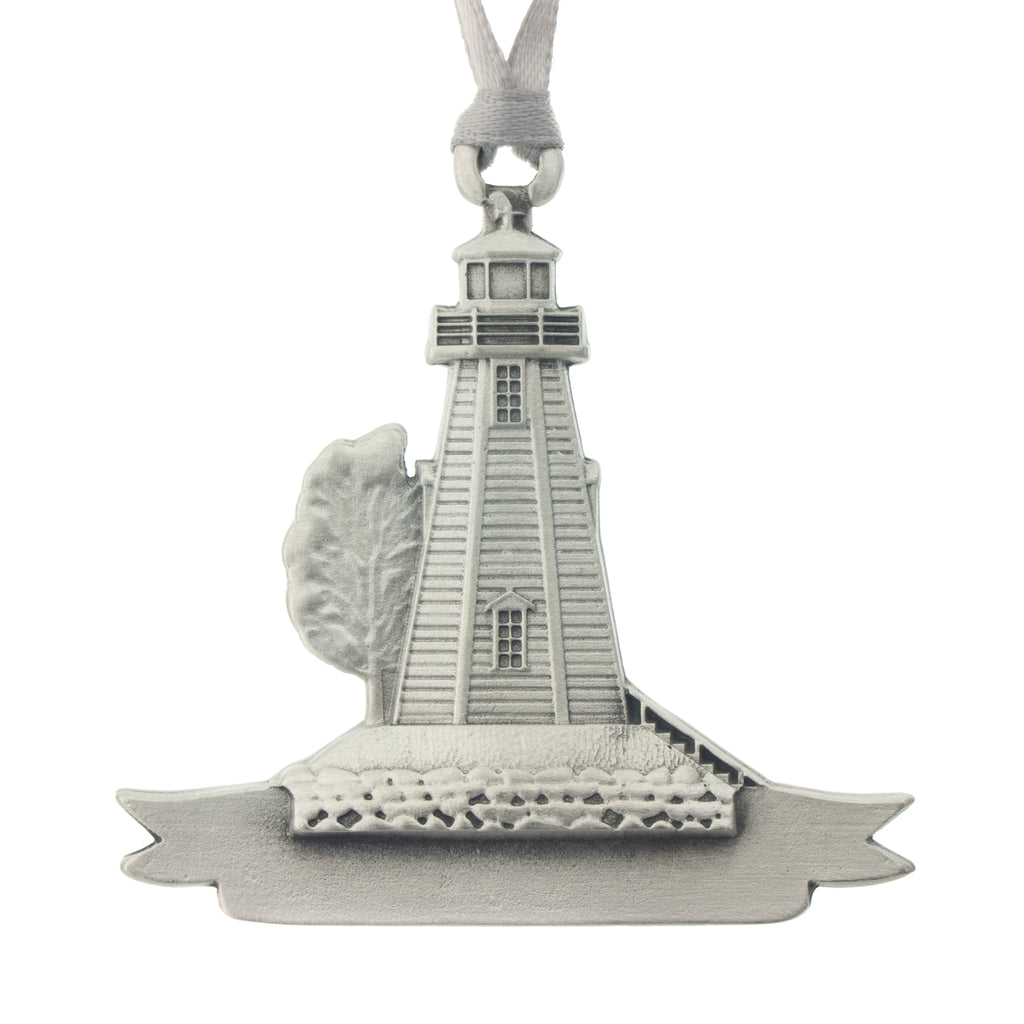 A lighthouse and tree over a small banner. Christmas Tree ornament. Made from Pewter. Silver ribbon. Made in Fredericton NB New Brunswick Canada
